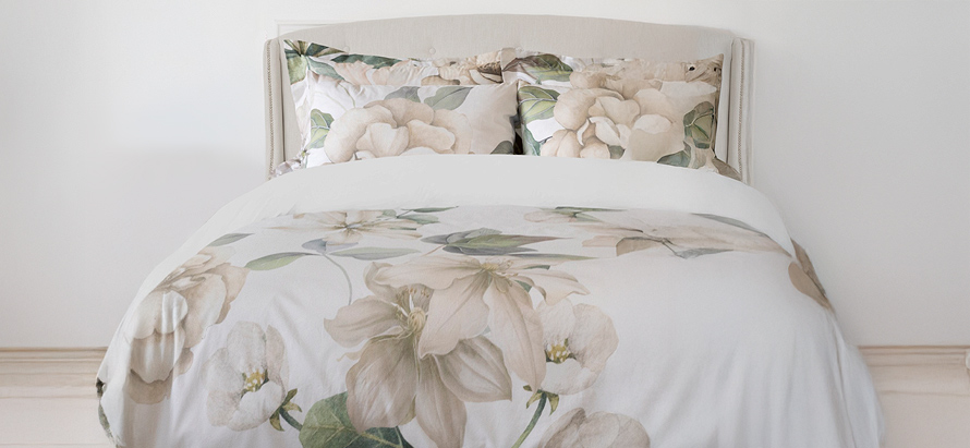 A neatly made bed with a floral-patterned duvet and pillows featuring large, soft cream and beige flowers, creating a calm and inviting atmosphere.